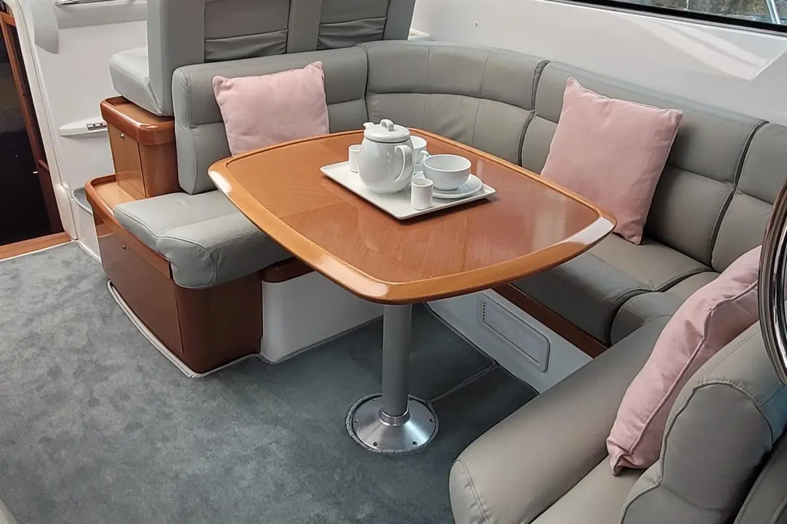 Modern boat interior featuring a grey leather seating area with pink cushions, a wooden table, and a tea set on a tray.